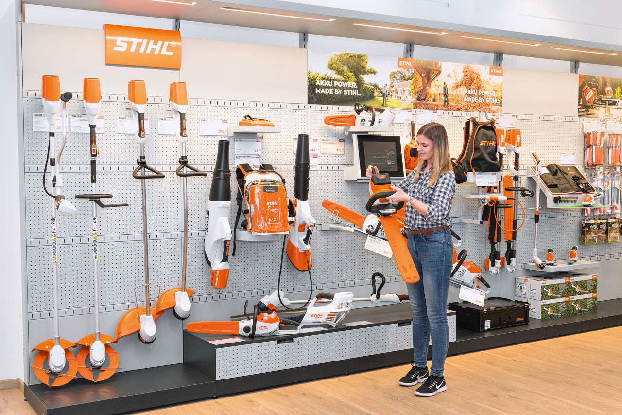 Mlada žena ispred prodajnog regala u STIHL specijalizovanoj prodavnici želi da besplatno testira STIHL lančanu testeru