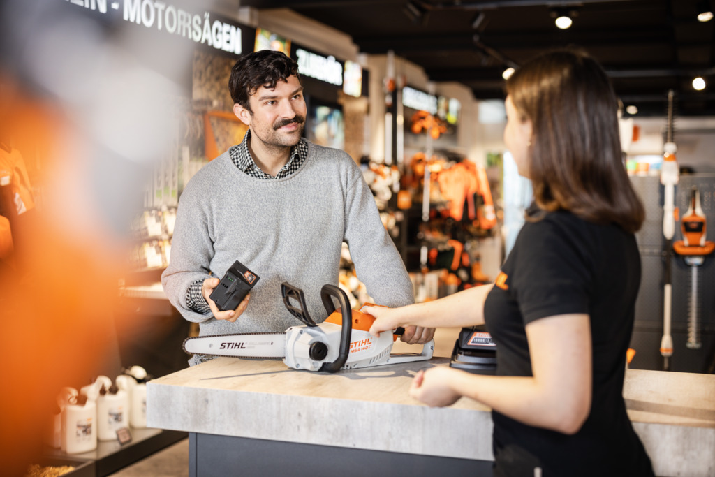 STIHL specijalizovani prodavac ispred regala savjetuje mladu ženu prilikom kupovine STIHL uređaja