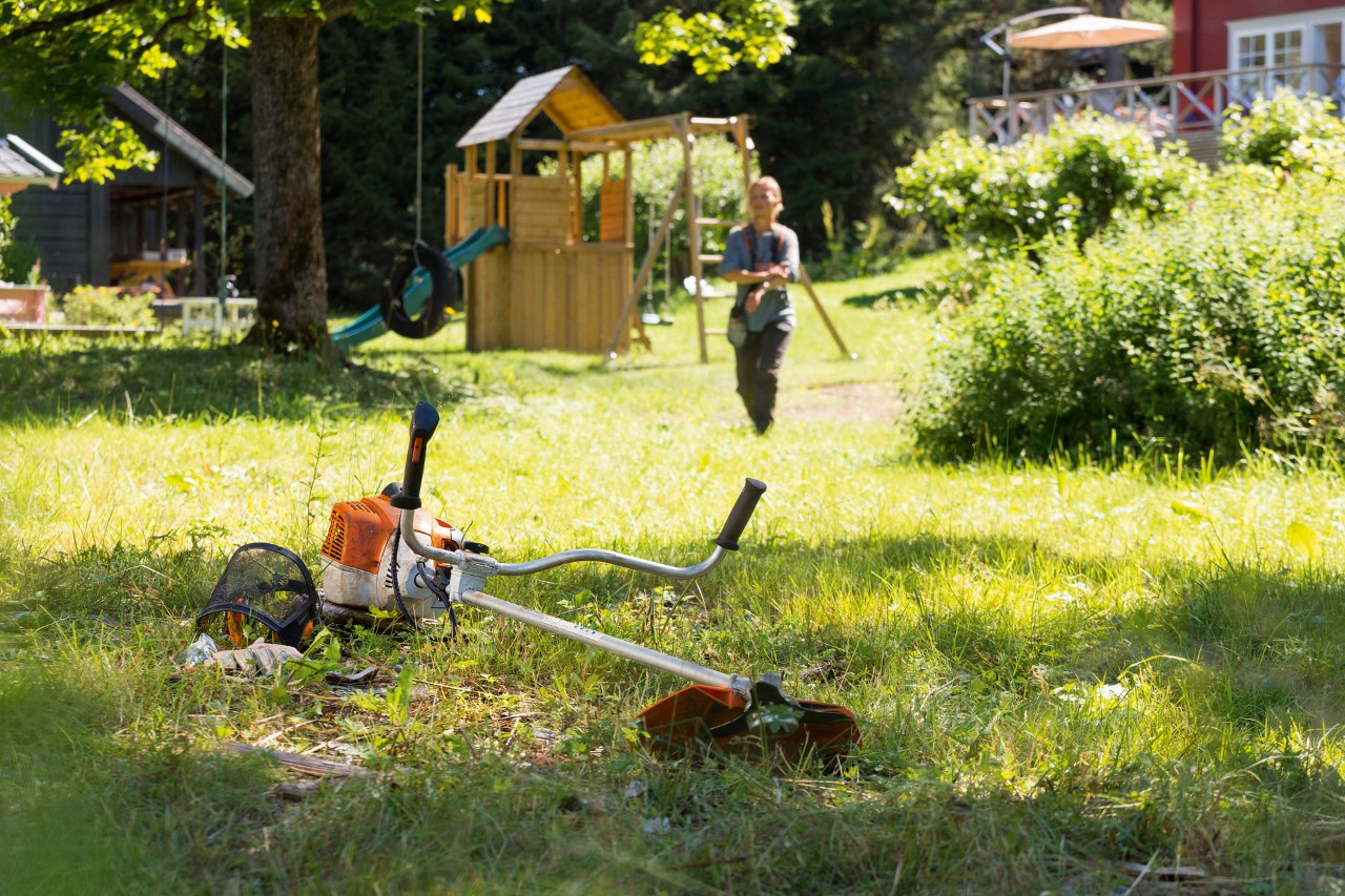 Motorna kosa STIHL FS 240 leži u travi, u pozadini se čovek priprema za održavanje